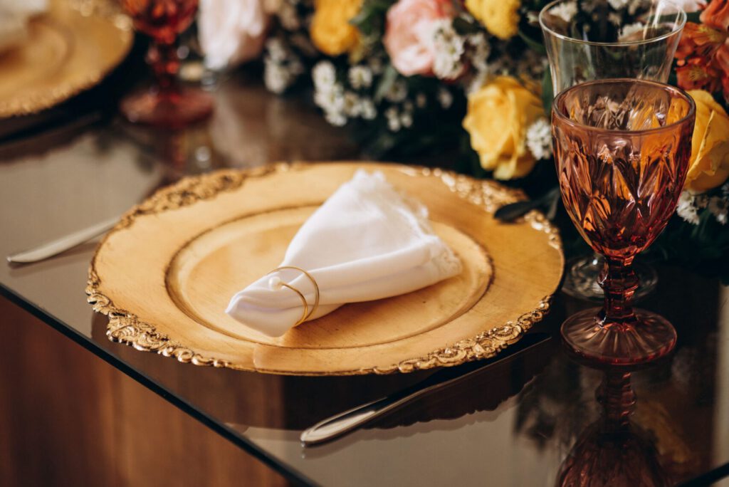 A sophisticated dining setup featuring golden plates on a glass table adorned with elegant floral arrangements.
